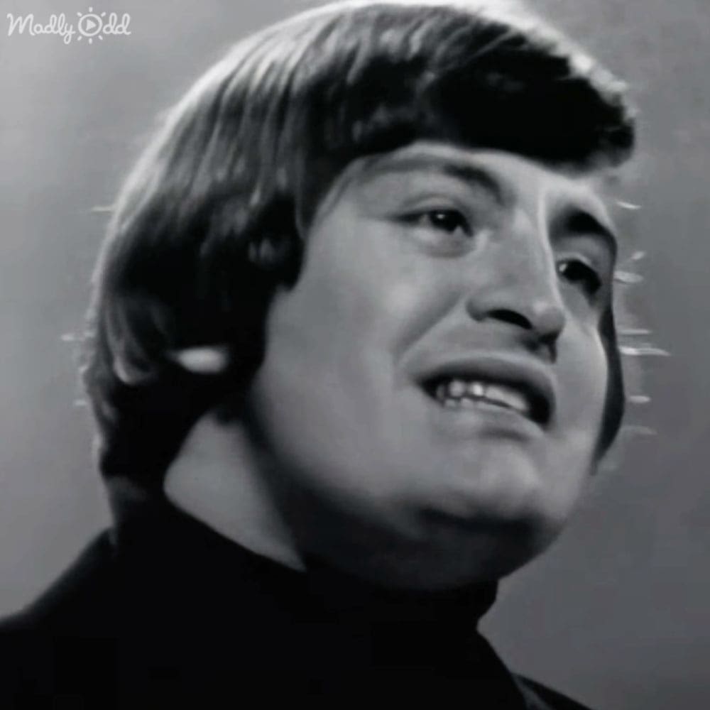 Adult male with short wavy hair, dark turtleneck sweater or high-collared shirt indoors.