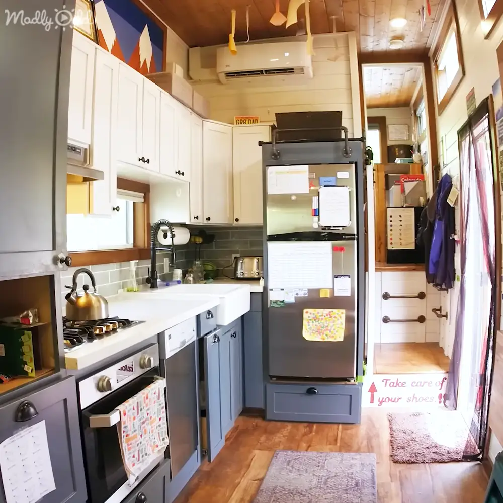 A kitchen interior with stainless steel refrigerator, white cabinets, gas stove, dishwasher, sink, and wooden flooring under natural light.