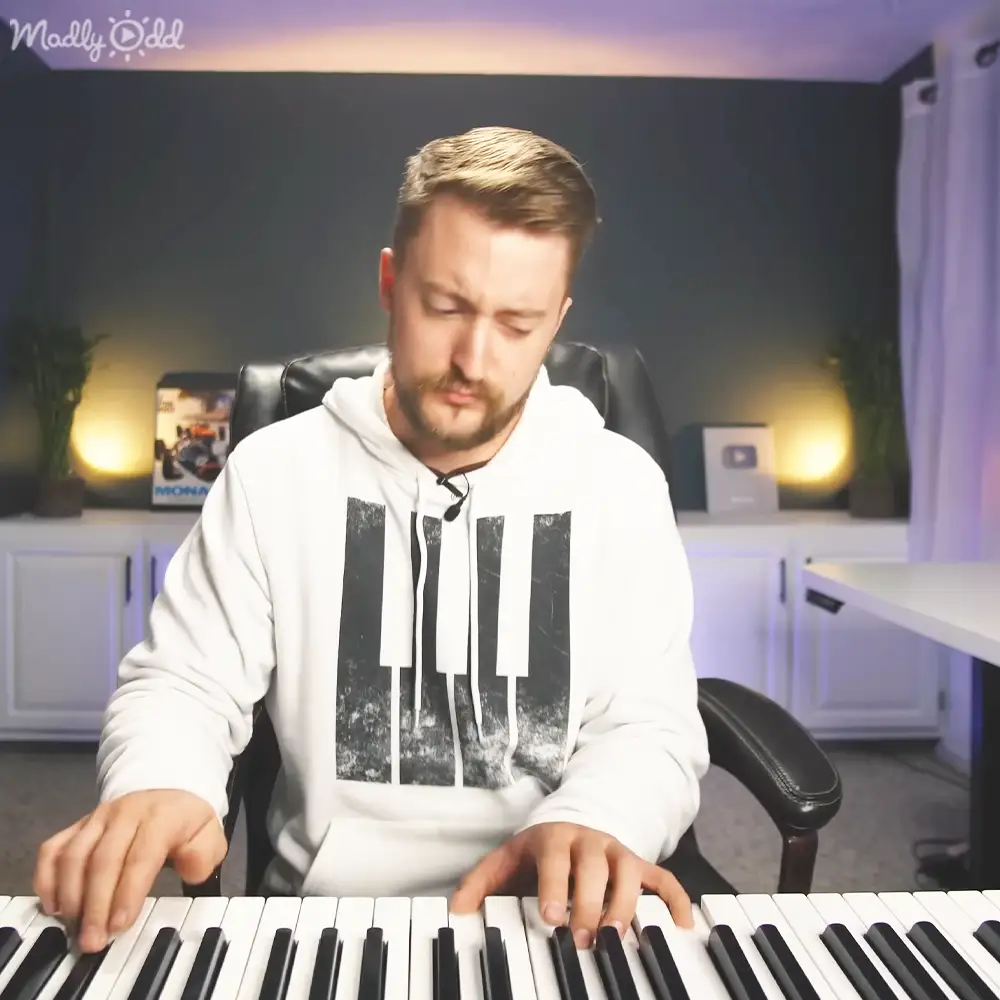 A young adult male plays piano in a home studio with soft evening lighting.
