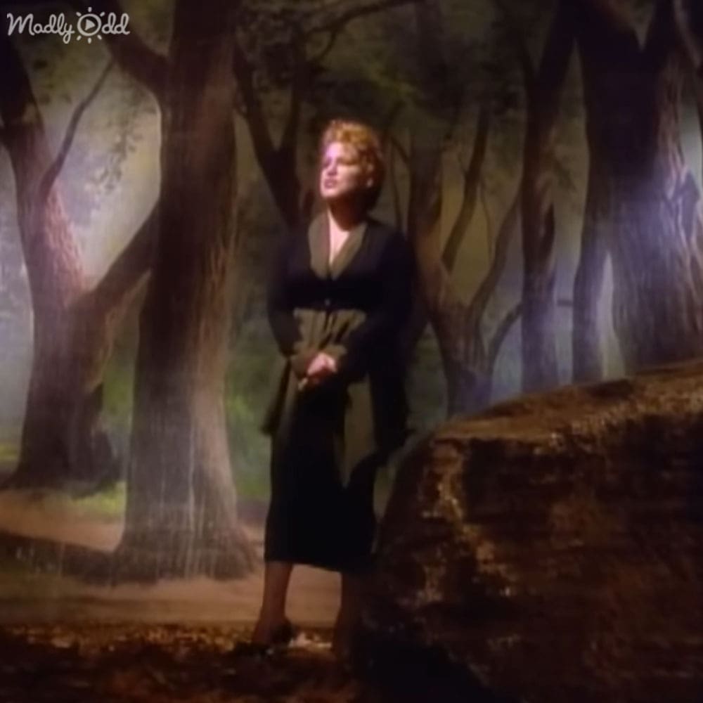 Adult female in an outdoor forest setting wearing a long-sleeved dress with a fitted bodice and loose skirt, knee-length, earth tones dominating the scene
