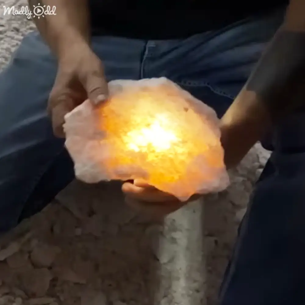 Adult male in jeans outdoors at night, glowing Himalayan salt lamp emitting warm light on sandy surface