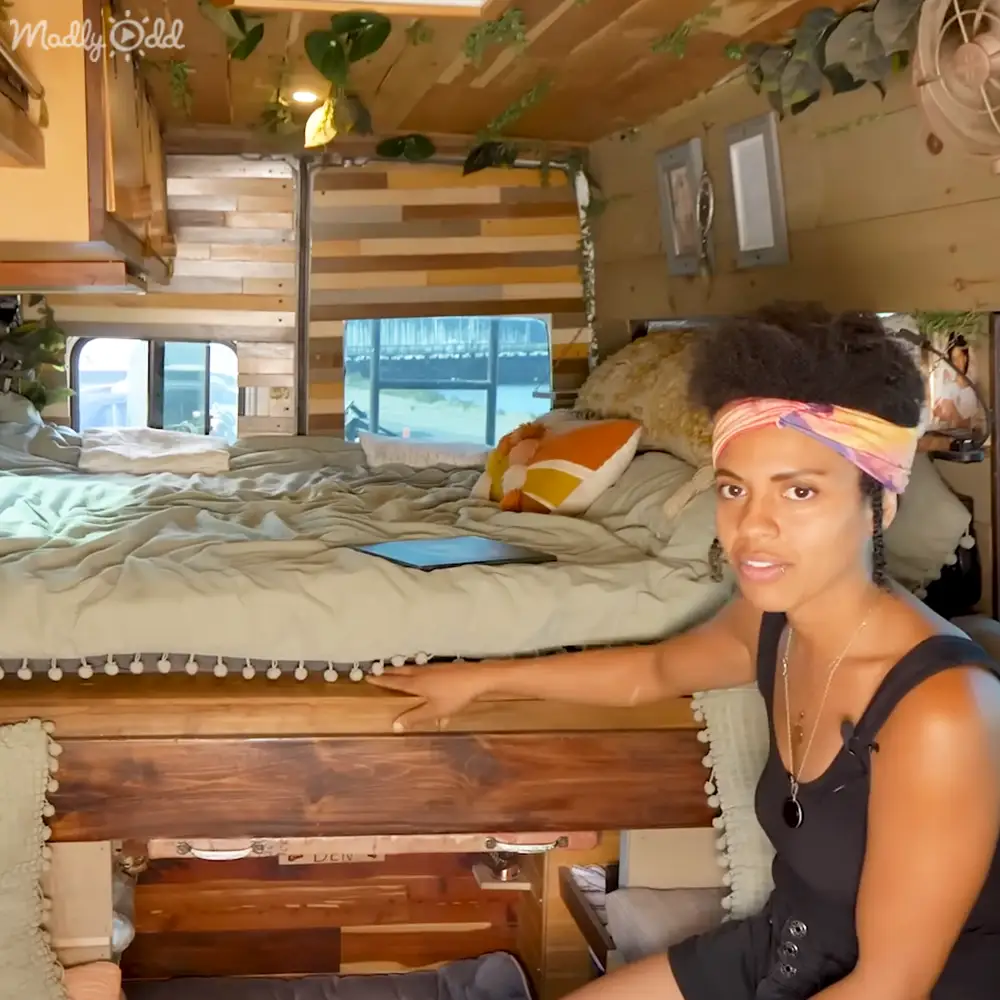 Young adult female wearing a black sleeveless top with buttons and ruffled detail, inside an RV interior with green bedding and wooden bunk beds.