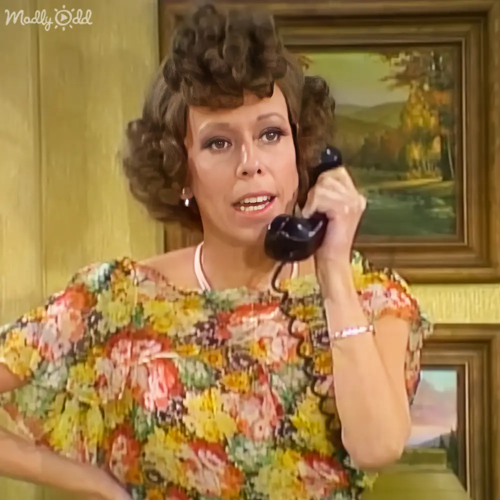 An adult female holds a rotary phone indoors with a framed landscape painting and wooden paneling, suggesting daytime natural lighting.