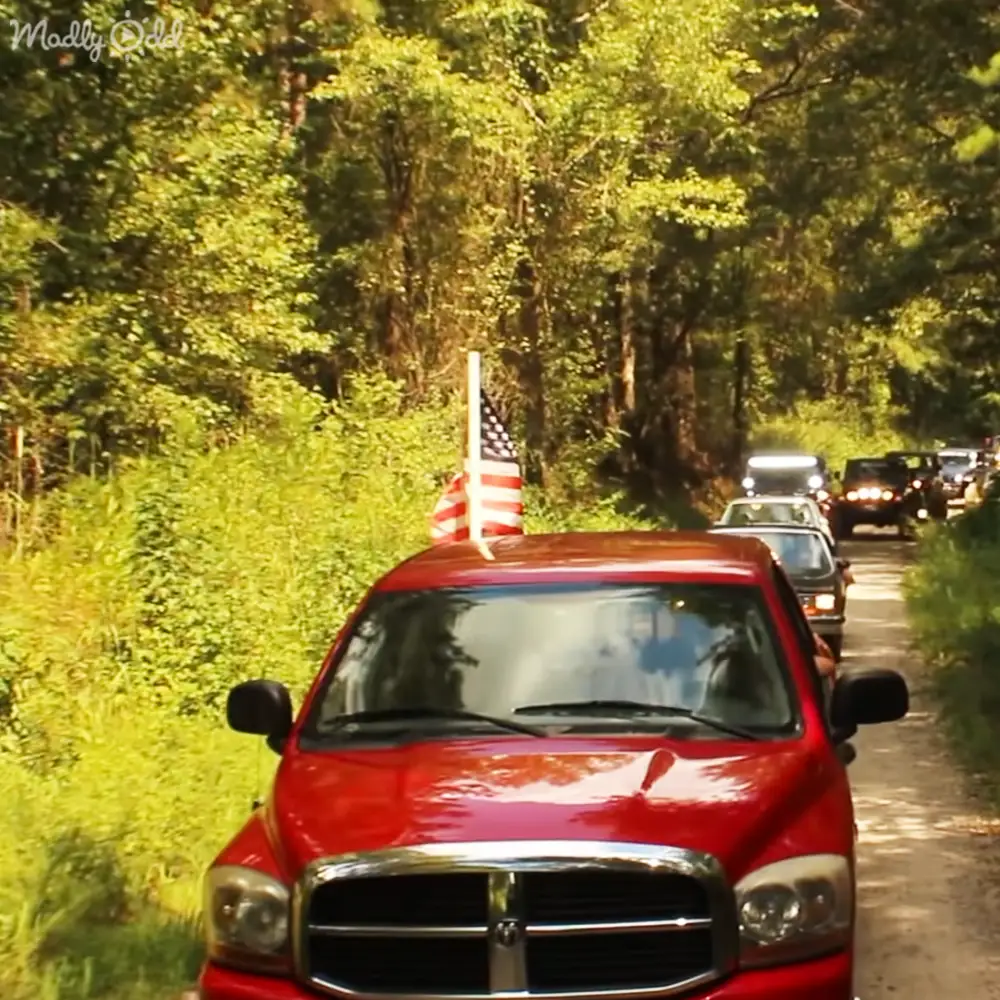 Red pickup truck with American flag parked in rural area surrounded by trees, late afternoon light