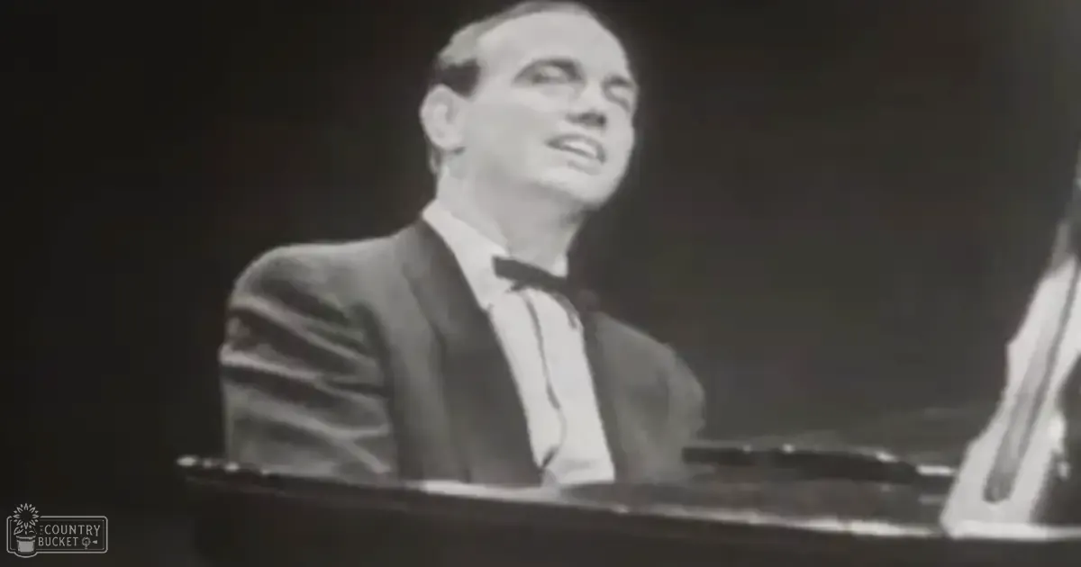 An adult male singer wearing a dark suit with vertical stripes indoors, possibly on stage or in a studio setting under focused lighting.
