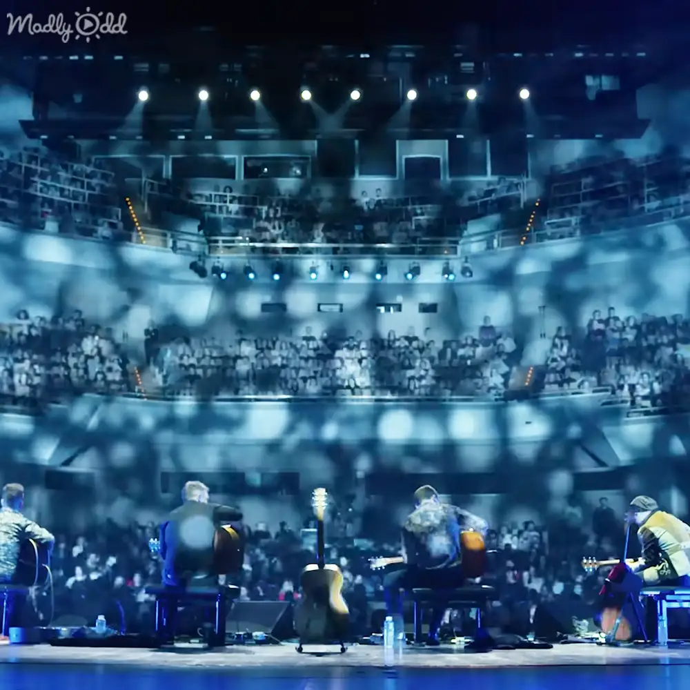 Musical performance in an indoor arena with rows of seating, stage lights illuminating musicians on a platform.