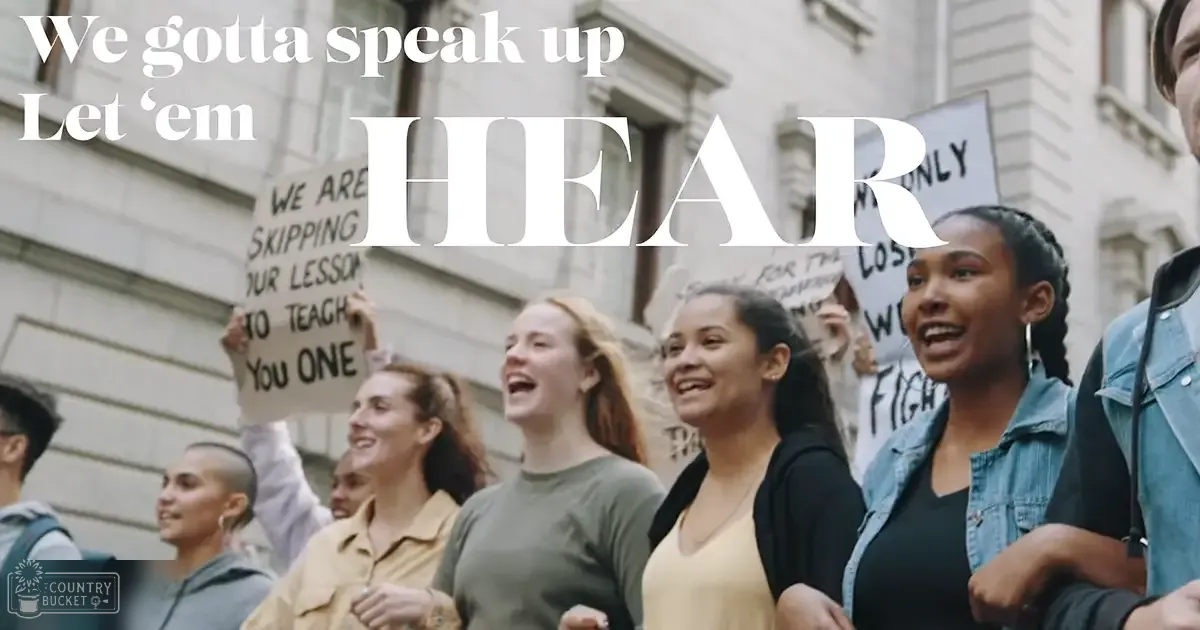 Group of young adults participating in a protest outside a classical building with signs reading 'WE ARE SKIPPING OUR LESSON TO TEACH YOU ONE' and 'ONLY'.