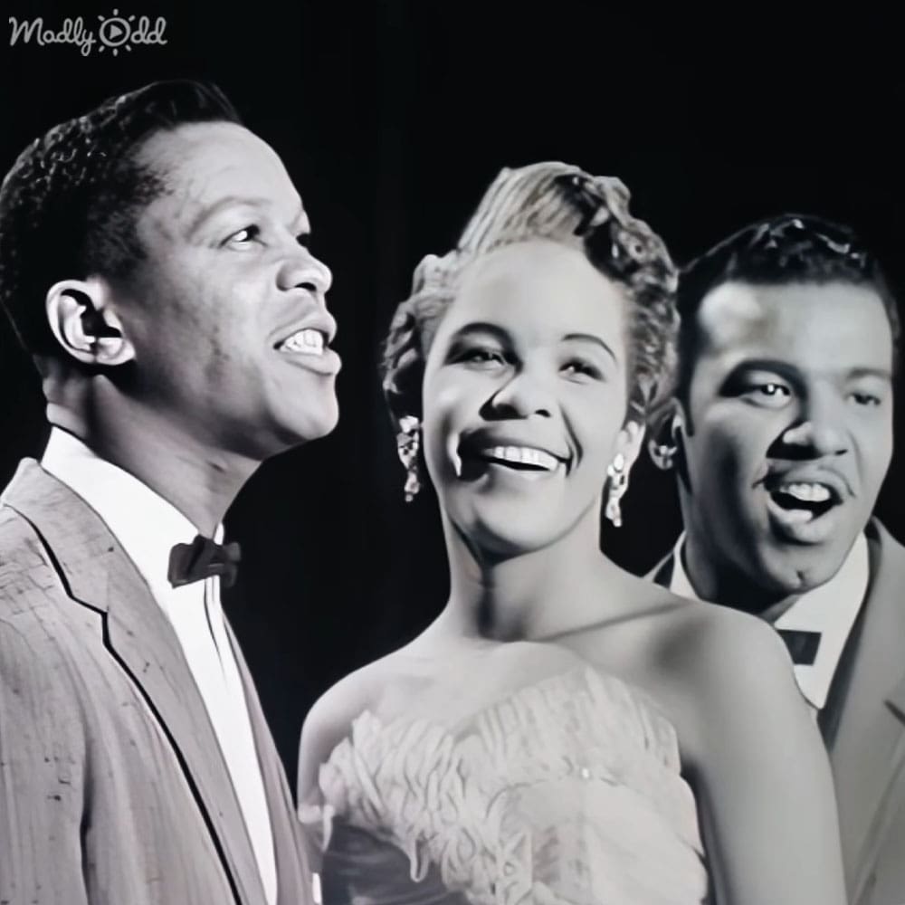 Three adults in formal attire indoors with dark background, no specific season or time of day indicated by lighting.