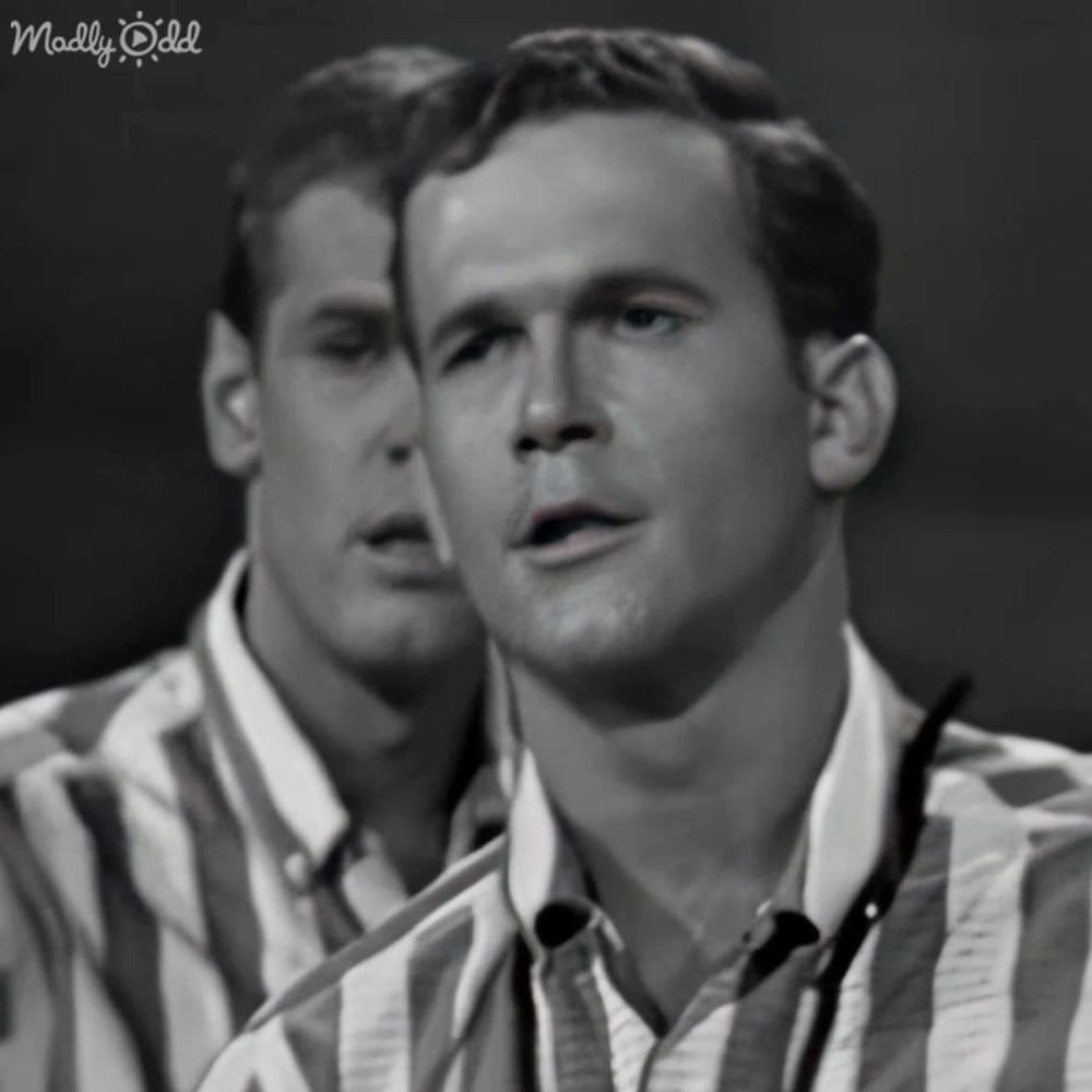 Young adult male in striped shirt, mid-20th-century style, indoor setting with plain background and even lighting.