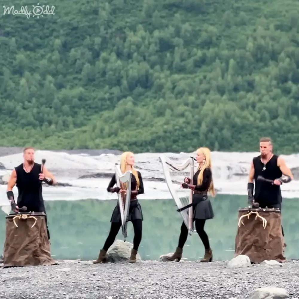 Adult males and females performing in an outdoor natural setting with lush greenery, riverbank or lakeside backdrop, midday light.