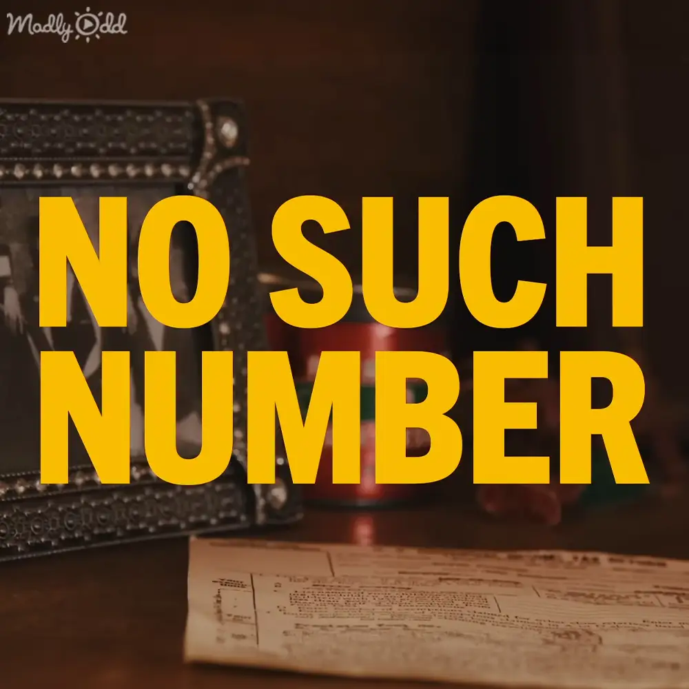 An open telephone directory with 'NO SUCH NUMBER' bolded lies on a wooden table, surrounded by vintage-style rotary phones and red objects, likely in an indoor home office or study area with warm artificial lighting at evening or night time.