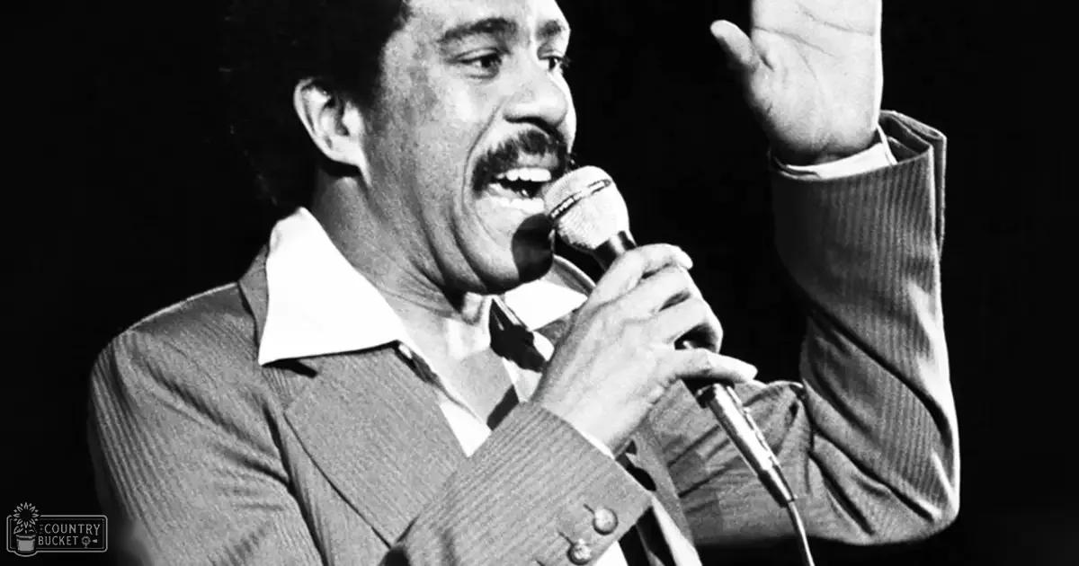 A middle-aged male singer dressed in a mid-20th-century style striped suit jacket over a white collared shirt with a bow tie, holding a microphone on stage.