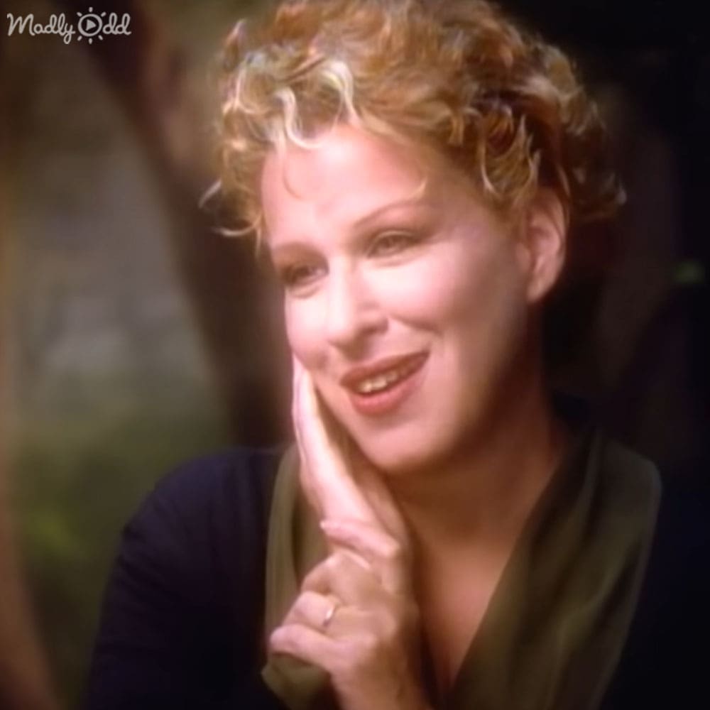 A middle-aged adult female wearing a loose, dark green long-sleeved top indoors with low light suggesting evening or night time.