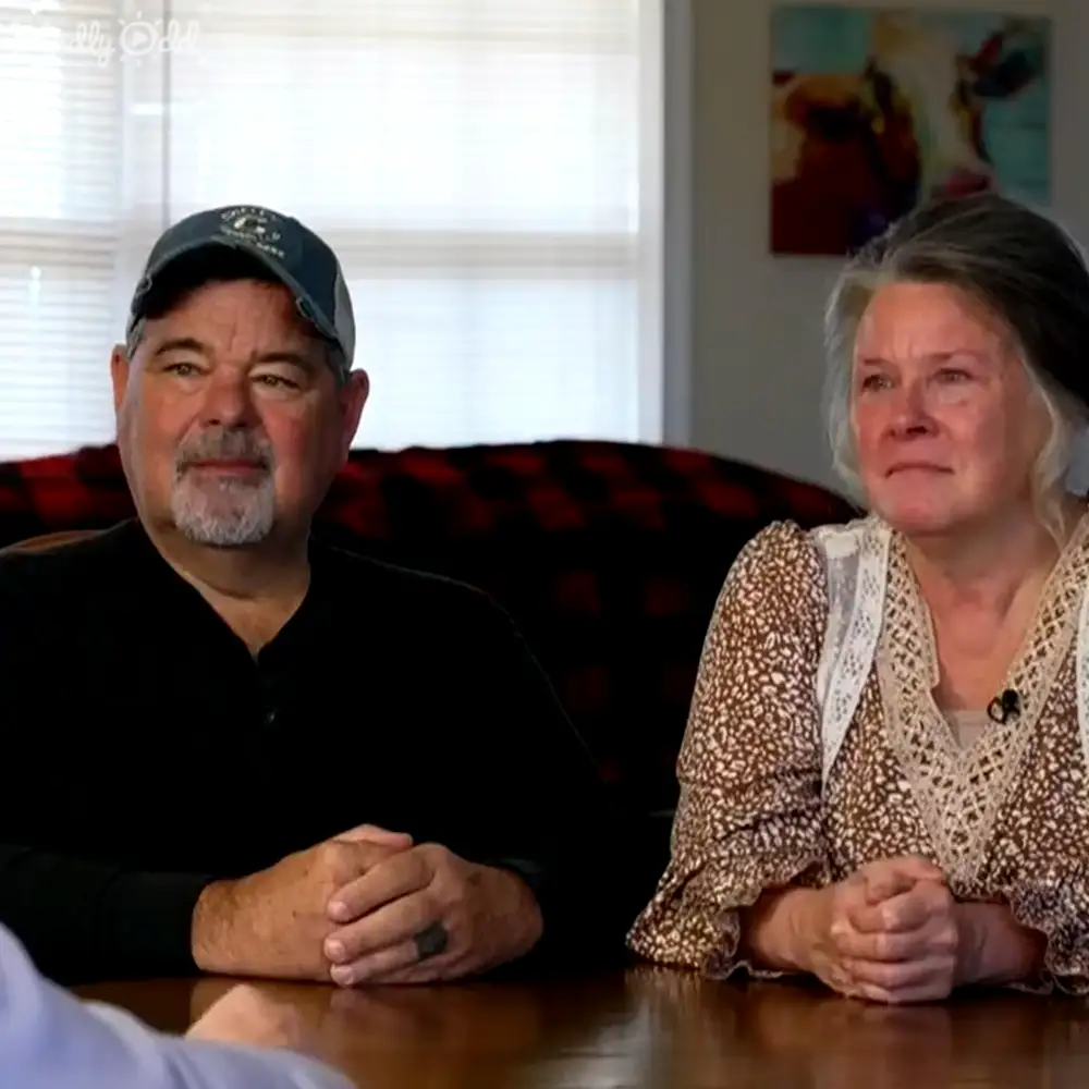 Older adult couple in a home setting with a dark-colored sofa and abstract artwork.