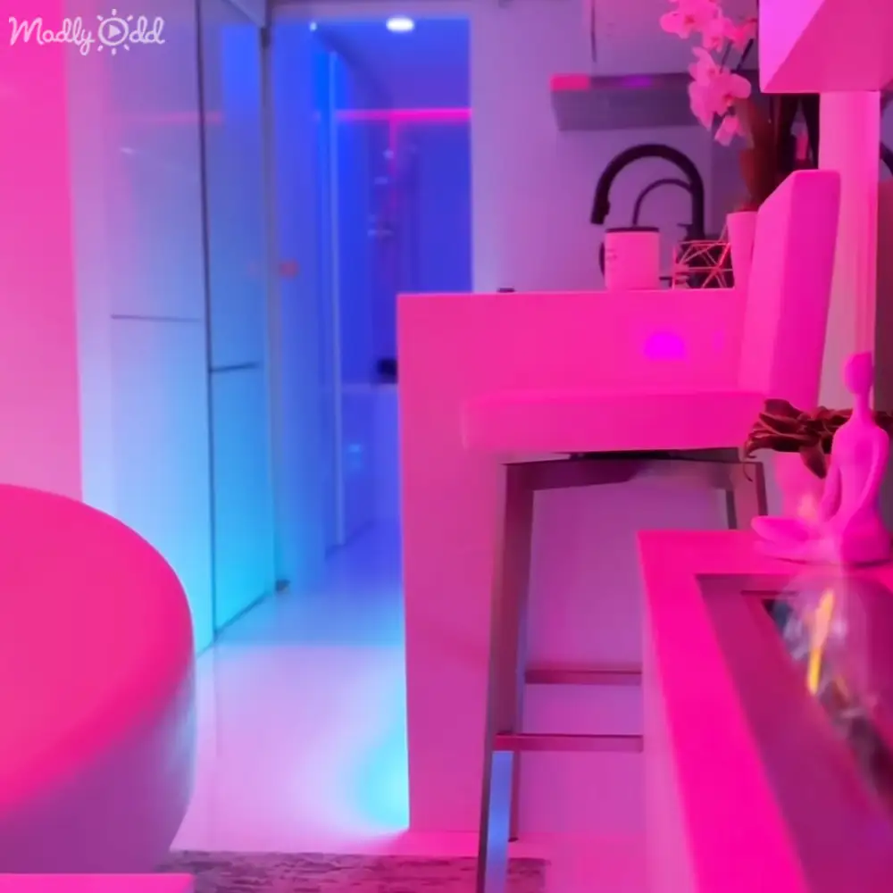 Indoor setting with vibrant lighting with a pink chair, white table with decorative items, and a shelf of ornaments.