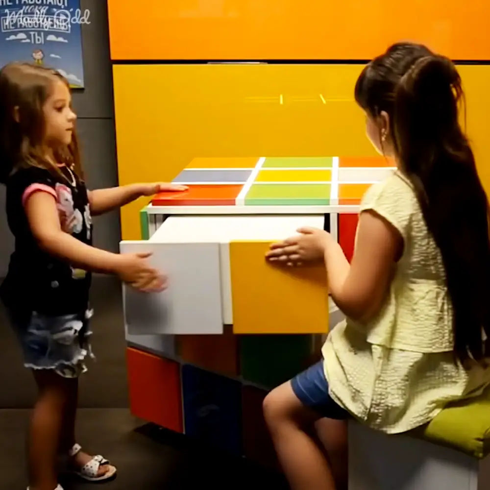 Two young girls interacting with a colorful display at an indoor exhibit or museum setting.