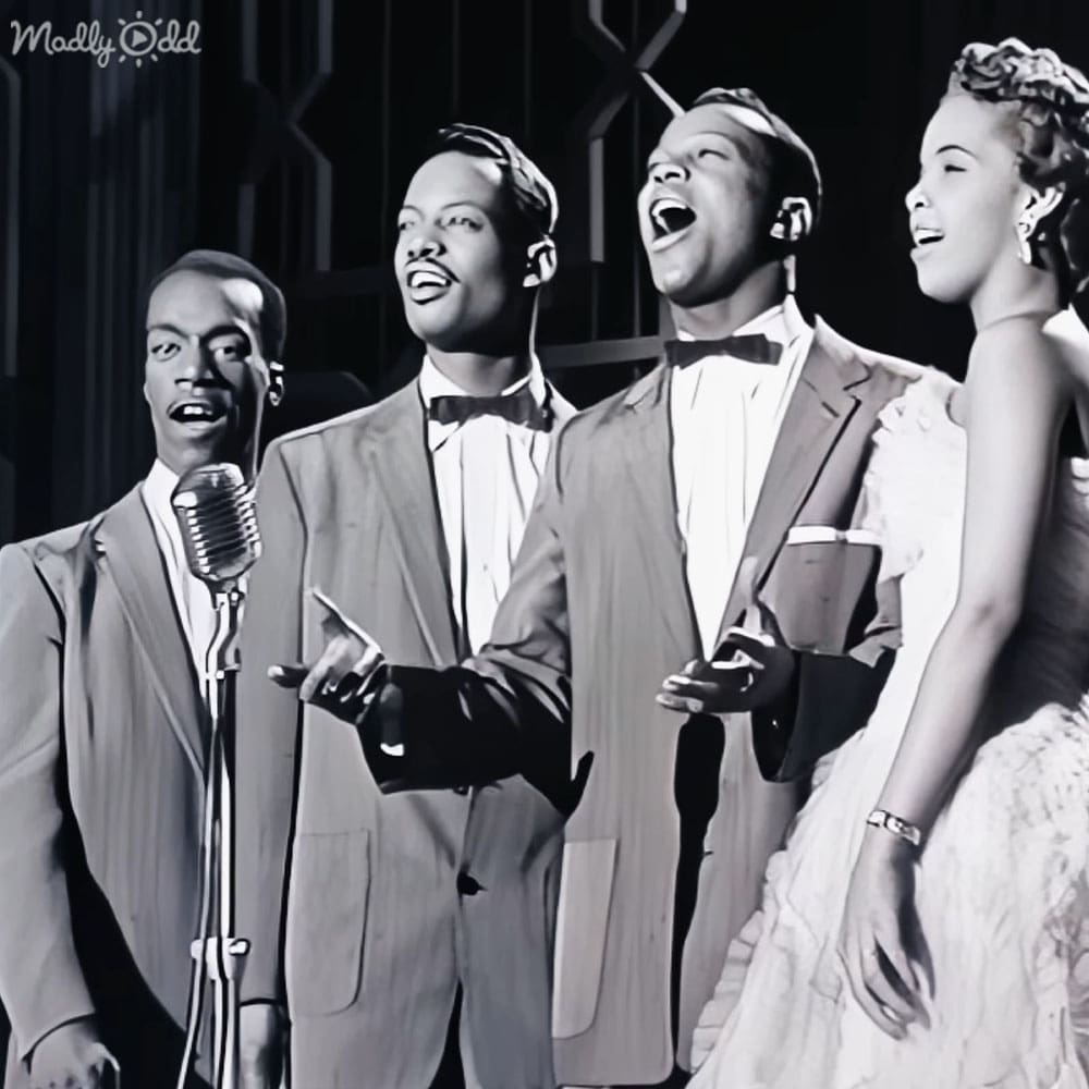 A mid-20th century musical performance group in formal attire on an indoor stage with dark curtains as the backdrop.