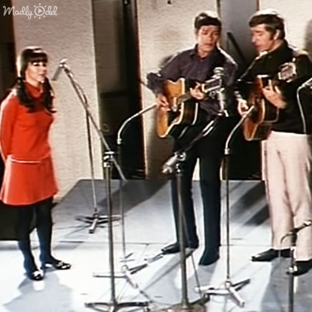 Musical performance in an indoor setting with microphones and neutral-colored walls, daytime lighting.
