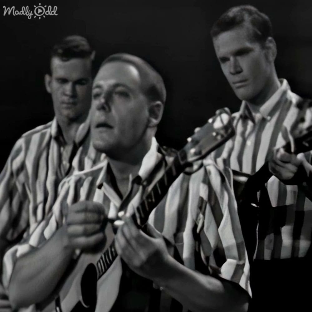 A group of adult male performers wearing striped prison uniforms stand on a stage or performance area within what appears to be a prison, under controlled indoor lighting.