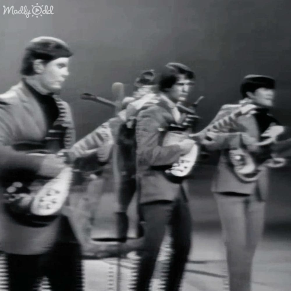 A musical performance from the 1960s or early 1970s with young adult males in similar style jackets on an indoor stage, muted tones typical of black-and-white photography.