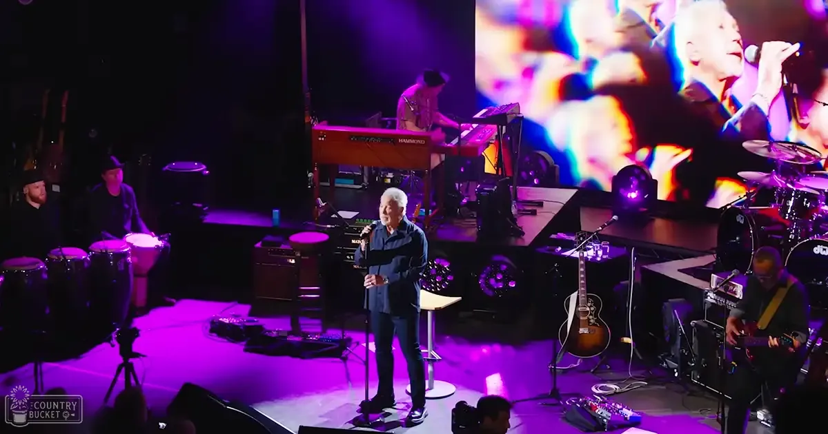 A middle-aged male singer performing at an indoor concert venue with a Hammond organ and musical instruments on stage under vibrant purple and white lighting.