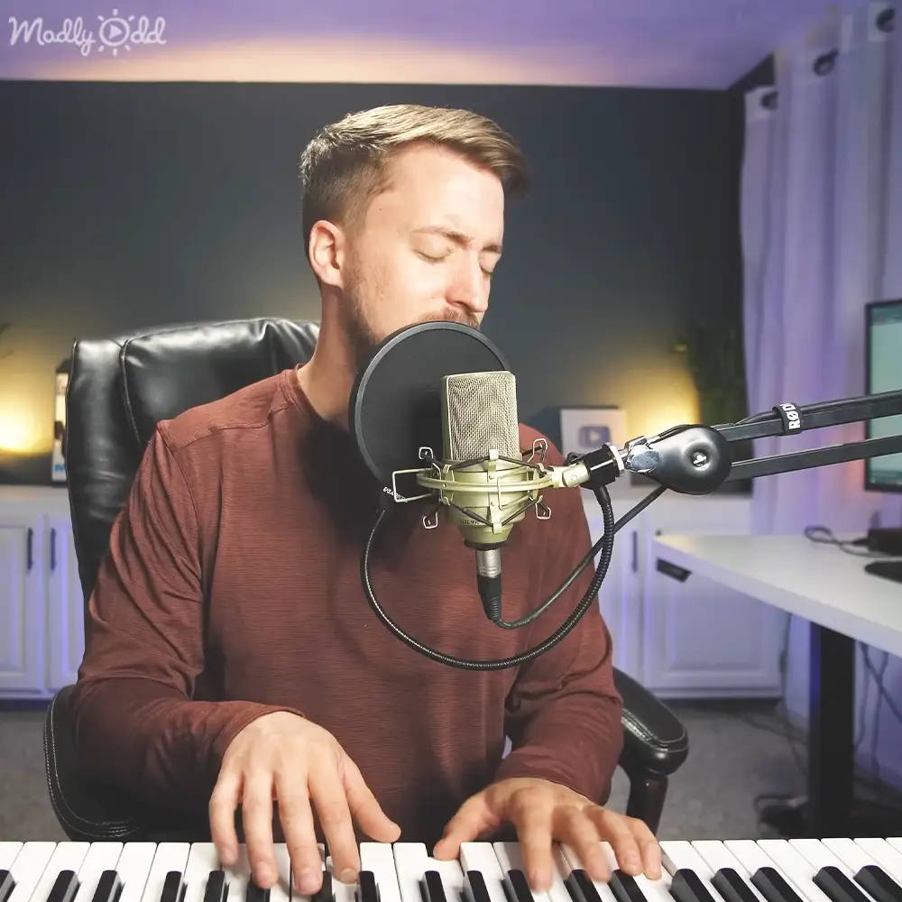 Young adult male in a home recording studio wearing a maroon long-sleeved shirt with a relaxed fit and modern casual style, surrounded by music production equipment.