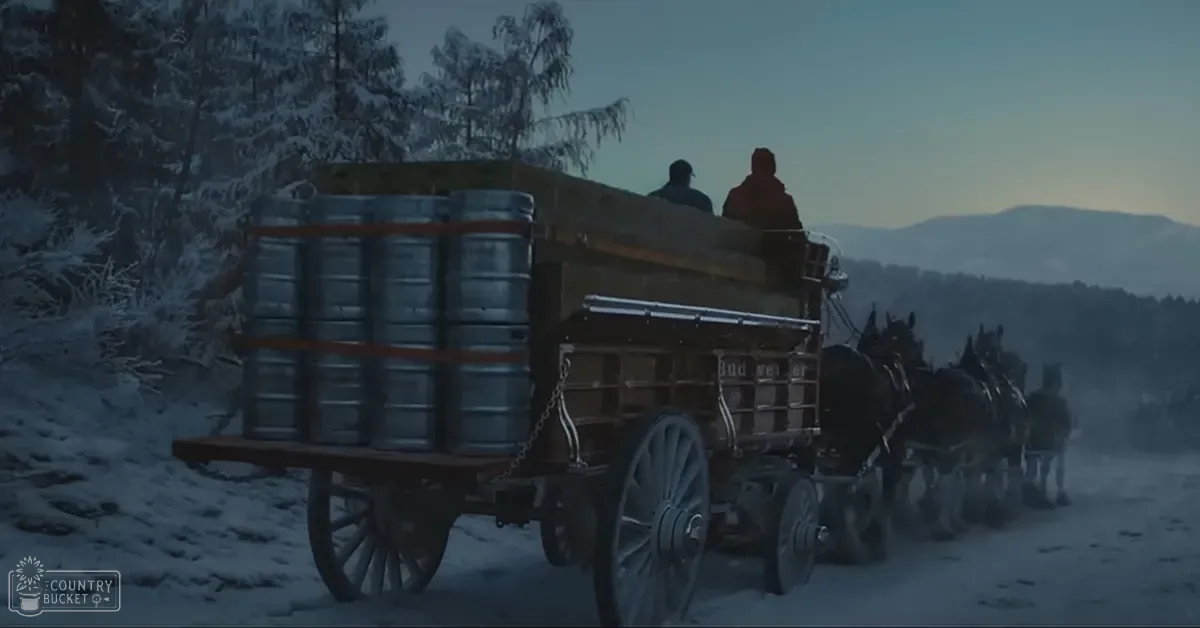 A horse-drawn wagon loaded with kegs in a snowy landscape with trees covered in snow and mountains in the background.