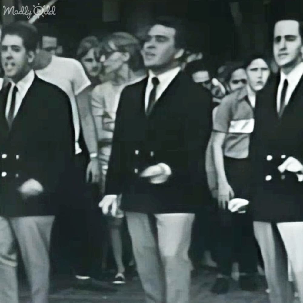 A group of adults dressed in dark suits standing outdoors, possibly during an evening event with artificial lighting.