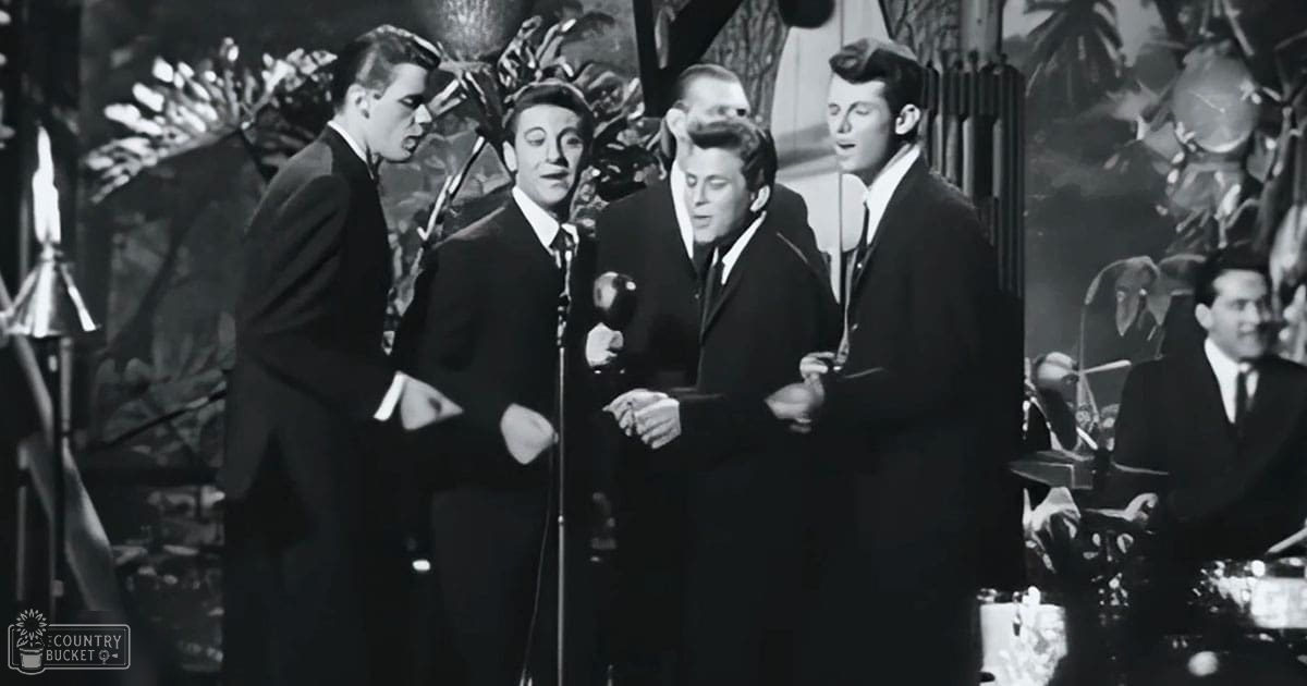 A mid-20th century musical performance scene with performers dressed in formal suits against a backdrop of tropical foliage under stage lighting.