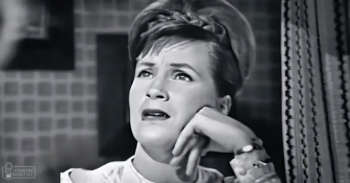 A middle-aged adult female holds a cigarette in an indoor setting, possibly a bathroom with tiled walls and a shower curtain visible.