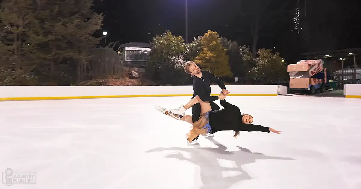 Adult male and female ice skating at an outdoor rink under artificial lights, surrounded by trees and a 'Krispy Kreme' food truck at night.