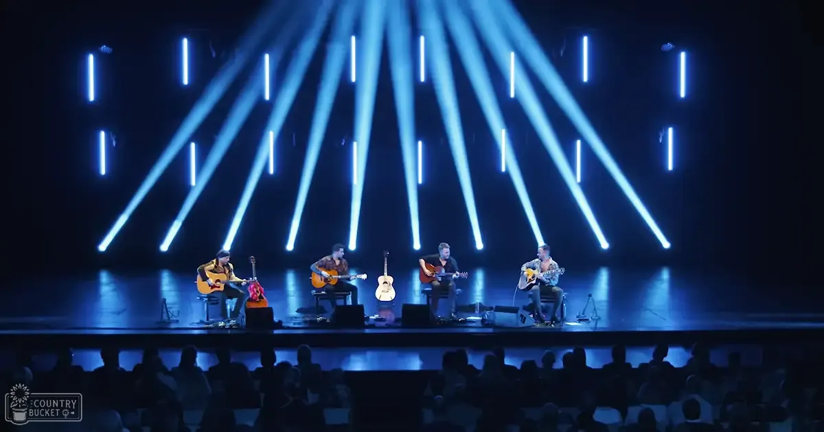 Musical performance in an indoor concert setting with adult males playing acoustic guitars and bright blue spotlights creating a dramatic effect at night.