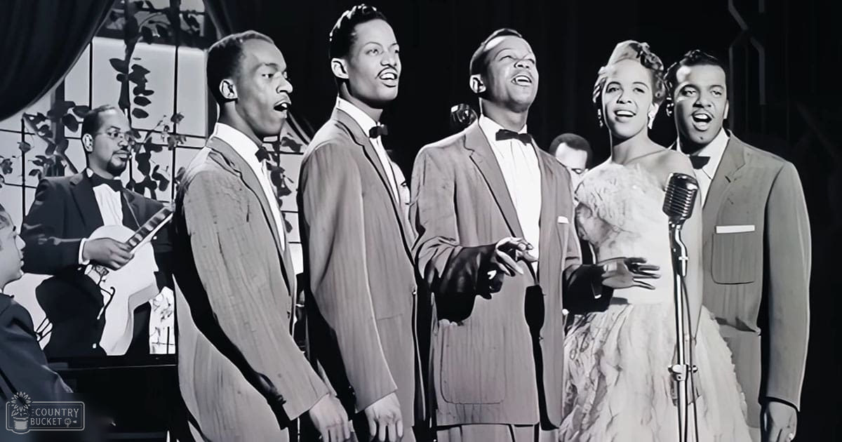 A musical performance scene with a young adult male in a dark suit, an adult male in light-colored suits holding microphones and wearing bow ties, and another adult female in an elaborate dress with ruffles or lace at the bottom of her skirt.
