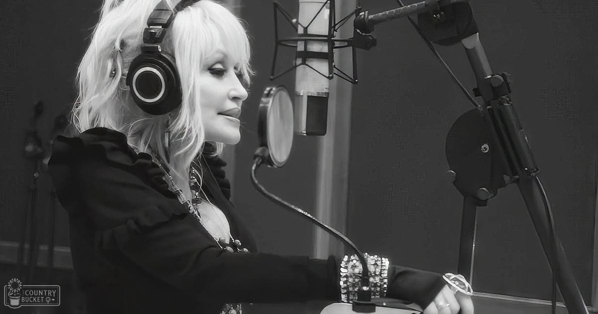 A middle-aged female in a recording studio, wearing a black ruffled jacket with vintage style, surrounded by audio equipment and soundproofing panels.