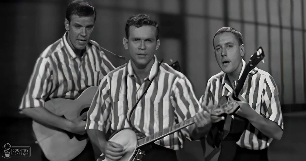 A prison escape scene from 'The Great Escape,' with young adult male performers in striped shirts, holding guitars against a backdrop of barred windows and concrete walls.