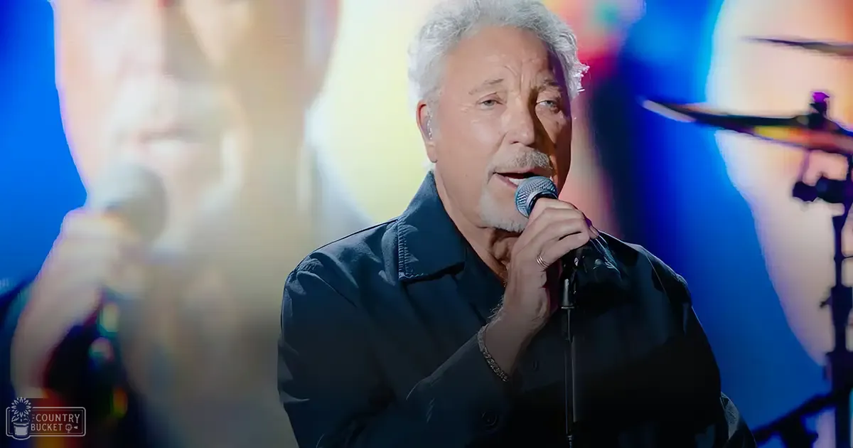 A middle-aged man singing into a microphone at an indoor concert setting, wearing a dark blue button-up shirt.