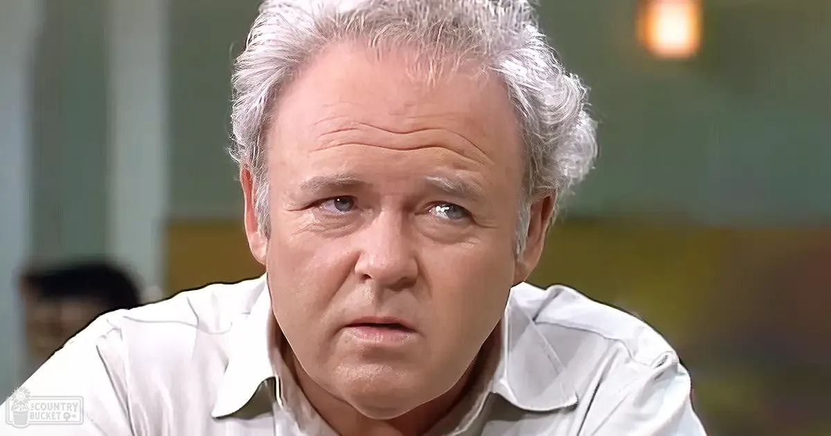 A middle-aged to older adult male wearing a light-colored collared shirt in an indoor setting with soft natural lighting.