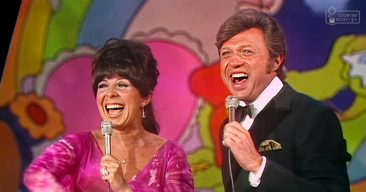 A musical performance scene with a female in a shiny pink dress and male in a dark suit, set against a vibrant floral background.