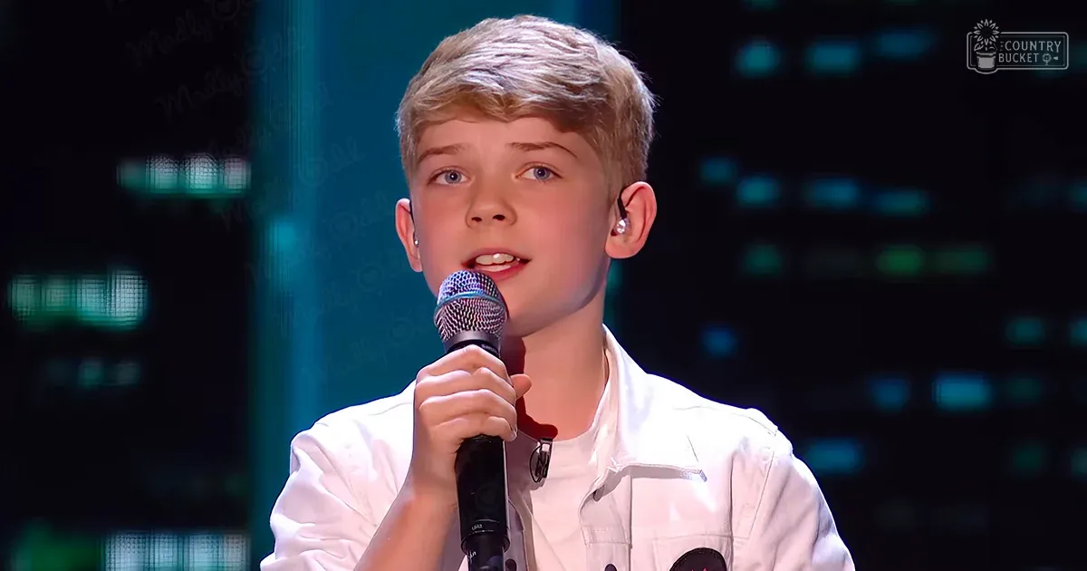 A young child wearing a white button-up shirt with an earpiece, performing indoors under stage lighting.