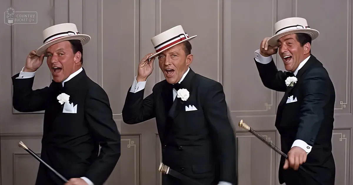 Formal indoor setting with three adult male singers dressed in black tuxedos and white shirts, holding canes, against a plain beige wall under bright stage lighting.