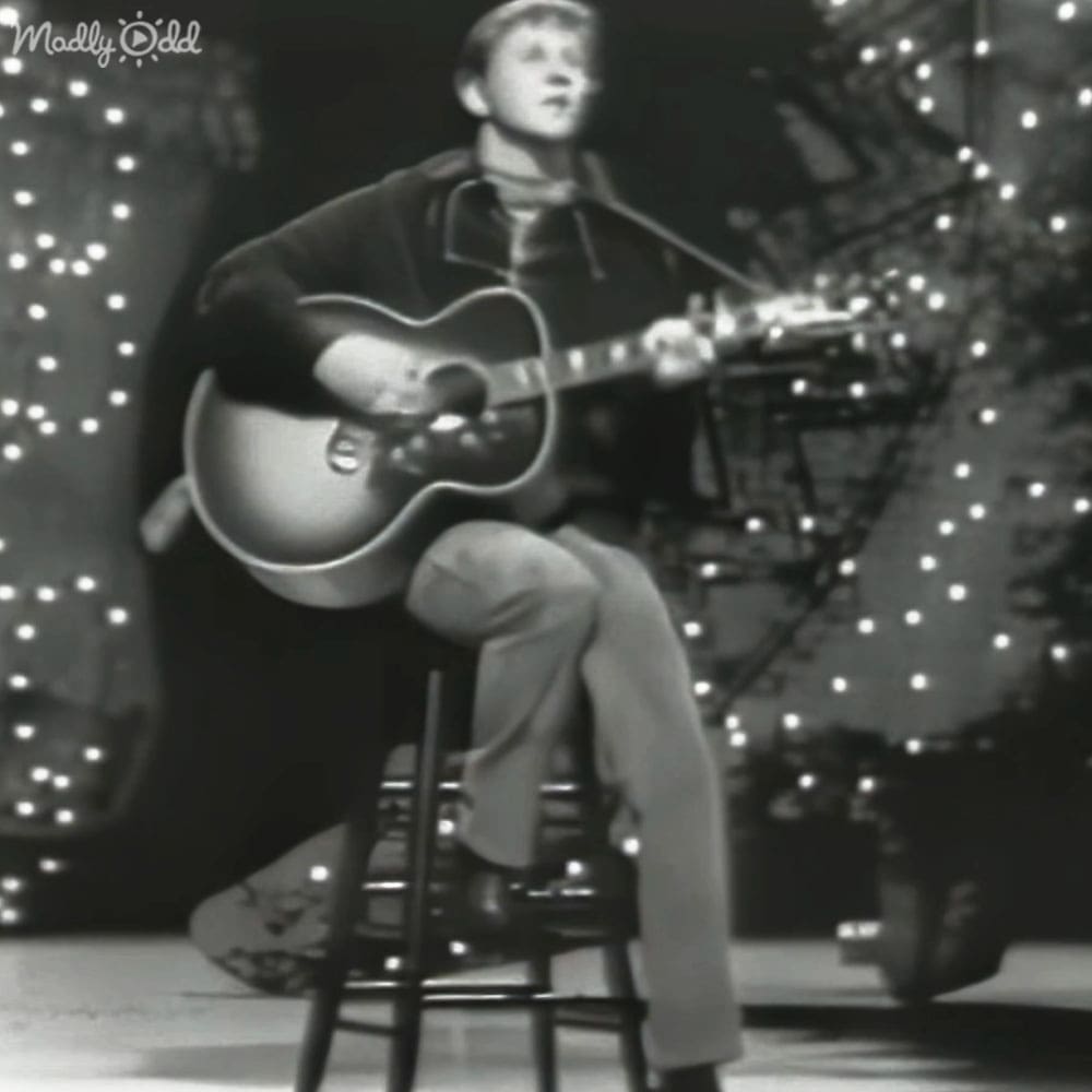 A young adult male performs on a stage decorated for a festive occasion with string lights and holiday decorations.