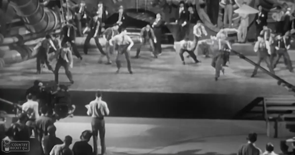 A dance performance set in an indoor theater with large mechanical structures resembling ship parts or industrial machinery as part of the backdrop, suggesting a maritime theme.