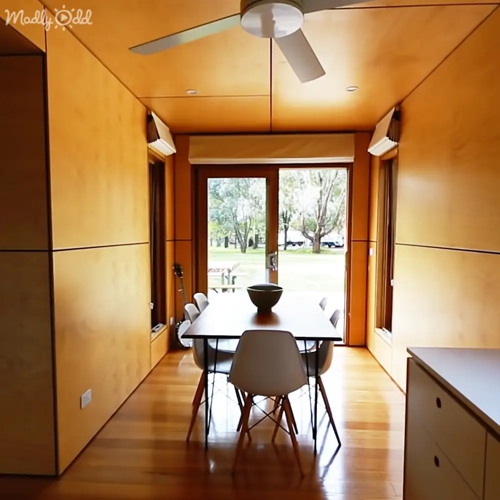 Modern dining area with sliding glass doors leading to an outdoor space during daytime, with wooden furniture, decor, and greenery outside.