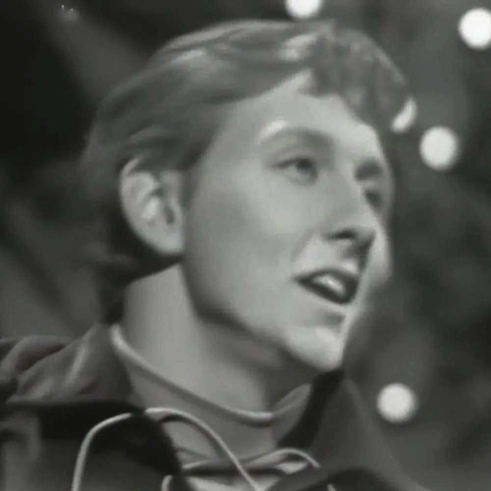A young adult female wearing a dark military-style uniform indoors with stage lighting.