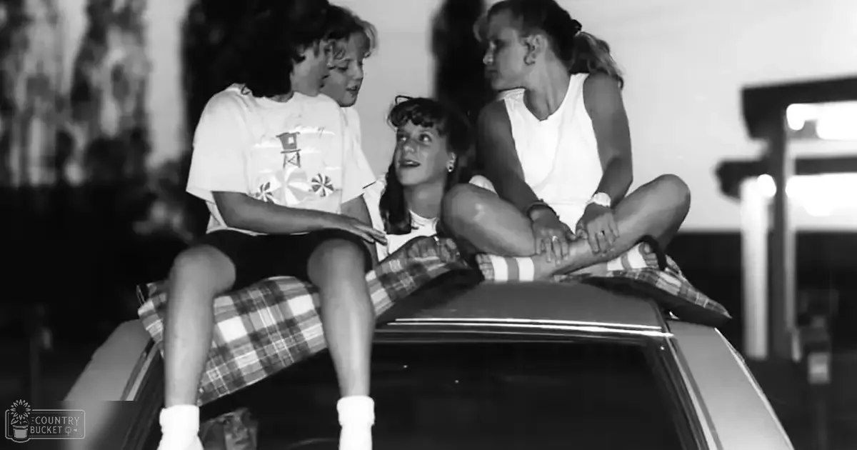 Three young children sitting on a car in an urban setting, wearing loose-fitting, patterned clothing; background includes buildings and hints of greenery.