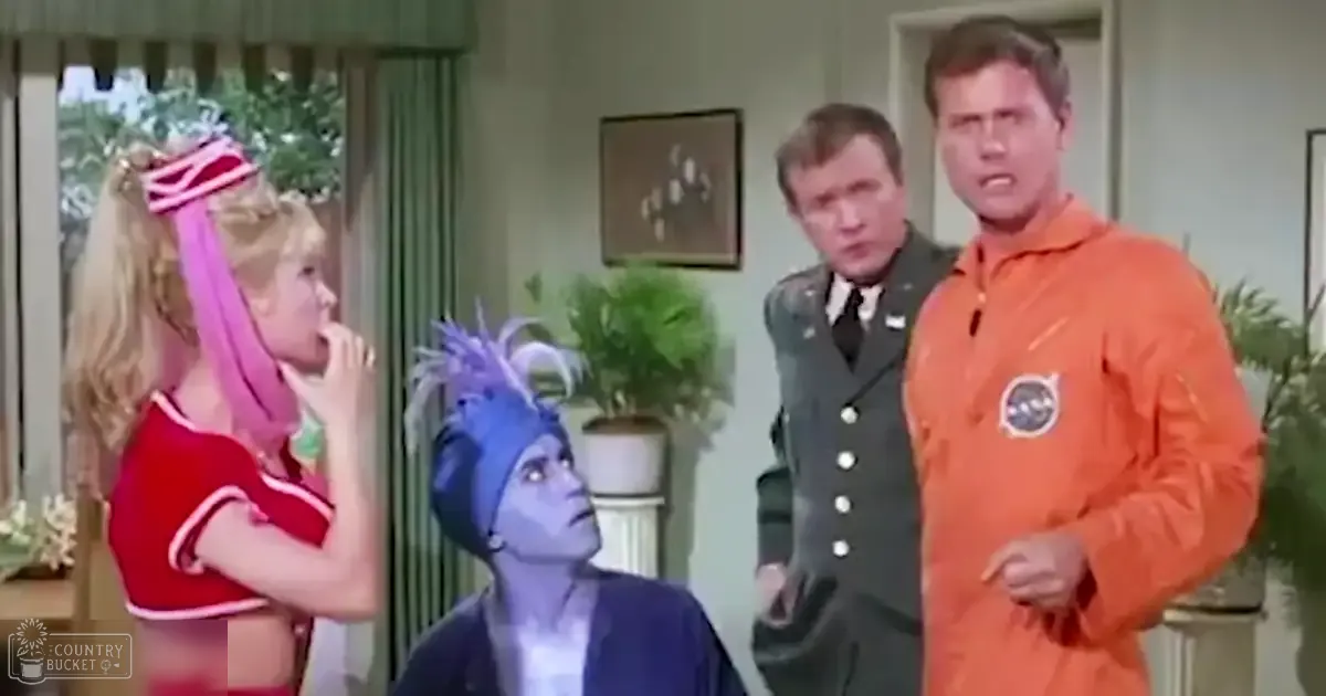 A young adult female wearing a red cheerleading outfit stands indoors with other adults dressed formally and casually. A potted plant and framed picture are visible in the background of what appears to be a living room.