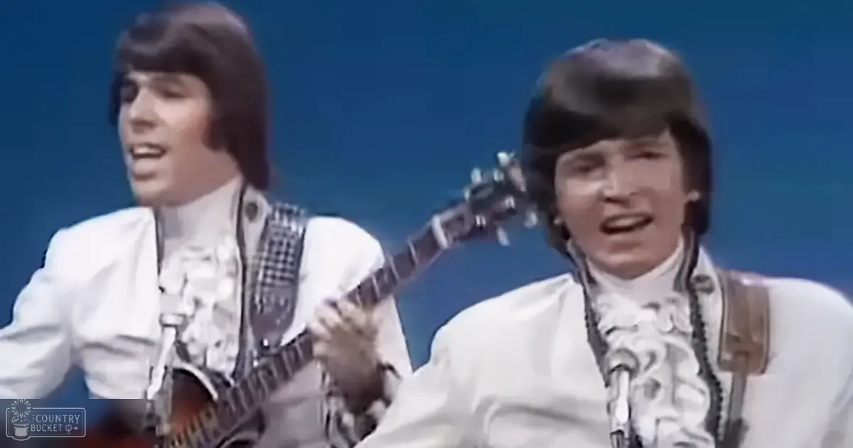 A musical performance scene with young adult males in white shirts and patterned ties holding instruments against a solid blue backdrop.