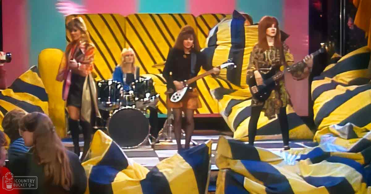 A musical performance in a vibrant indoor studio with children and adults, with patterned dresses and a drum set amidst striped bean bags.