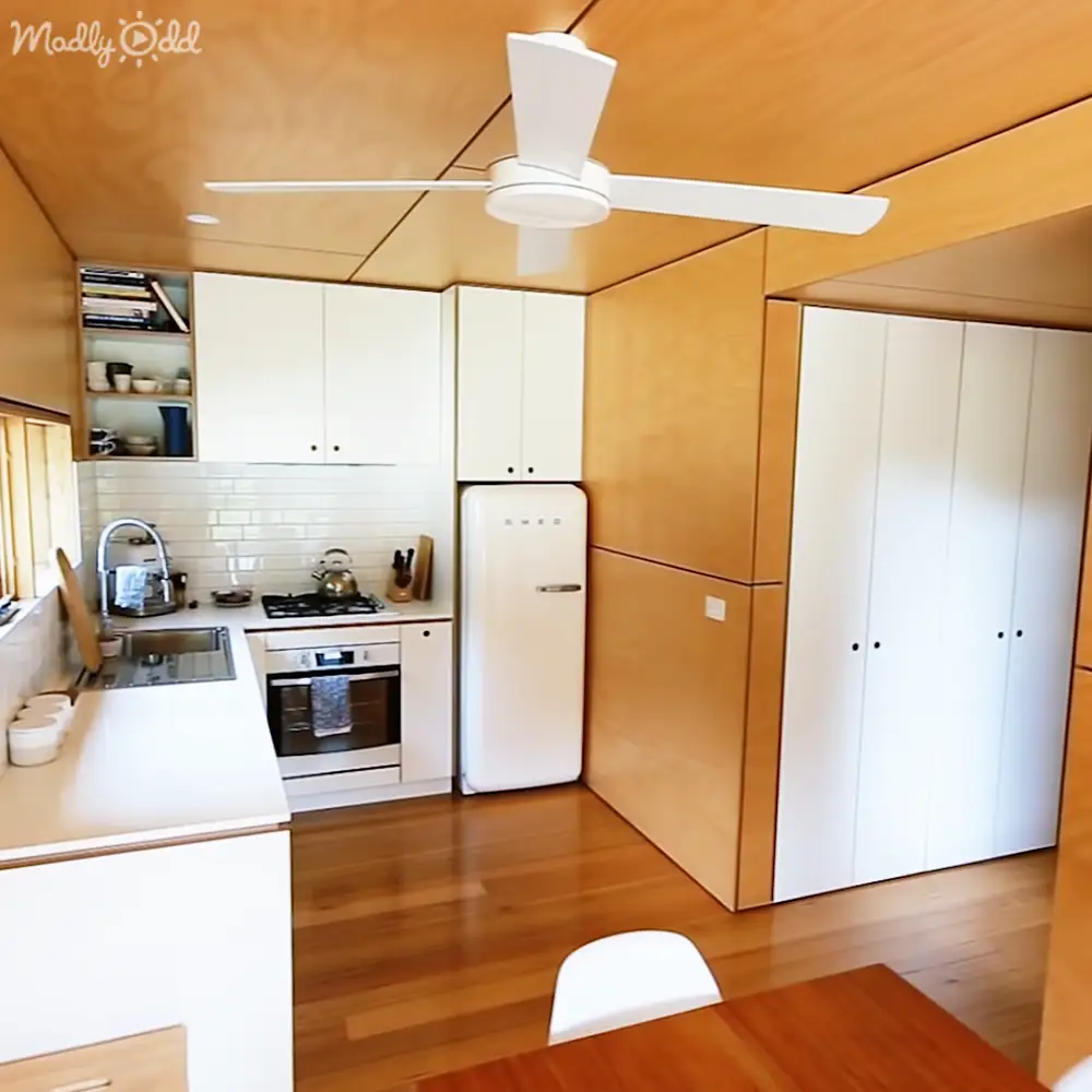 A modern kitchen interior with a retro-style refrigerator, gas stove, and white ceiling fan on a sunny day.