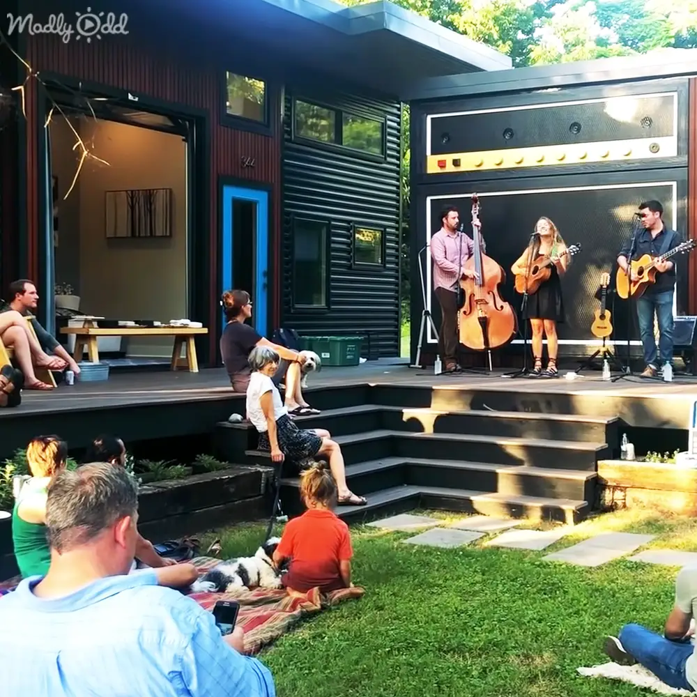 A small outdoor concert in a backyard with modern architecture, with a band playing live music under bright daylight.